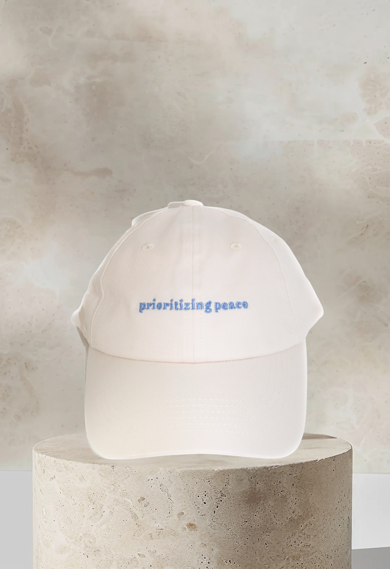 Cream dad hat with 'Prioritizing Peace' embroidered in light blue on front panel